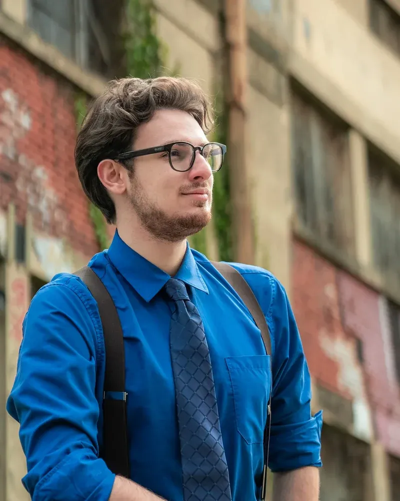 Charles Lindecker en chemise bleu roi, devant une friche industrielle.